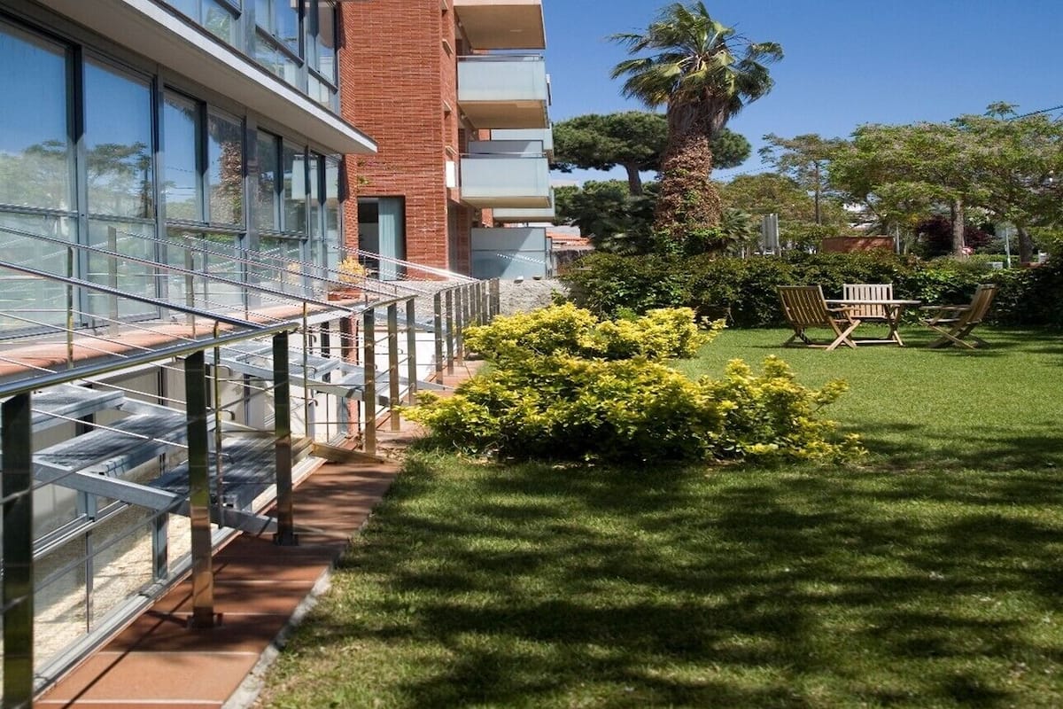 A modern building with a glass facade, a brick section, and a well-maintained lawn with outdoor furniture.