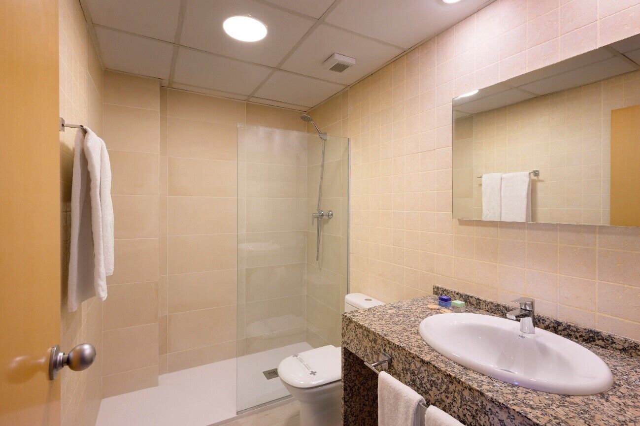 A bathroom with a glass-enclosed shower, a sink with a granite countertop, and a toilet.