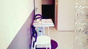 A narrow hallway with a white table and chairs, a purple chair, and a decorative glass panel with a rose pattern. - Beautiful studio center of Arbois (Arbois)