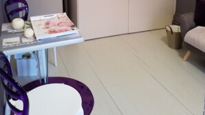 A room with a white wardrobe, a table with a floral tablecloth, purple chairs, a grey sofa, and a small trash bin. - Beautiful studio center of Arbois (Arbois)