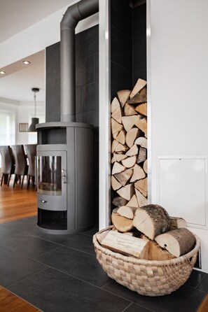 Ein modernes Interieur mit Kaminofen, Holzstoß und einem gewebten Korb auf dunklem Fliesenboden.