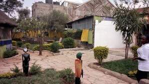 A courtyard with stone paving, a few trees, and a building with a corrugated metal roof. - Serengeti Gardens Hotel (Nairobi)