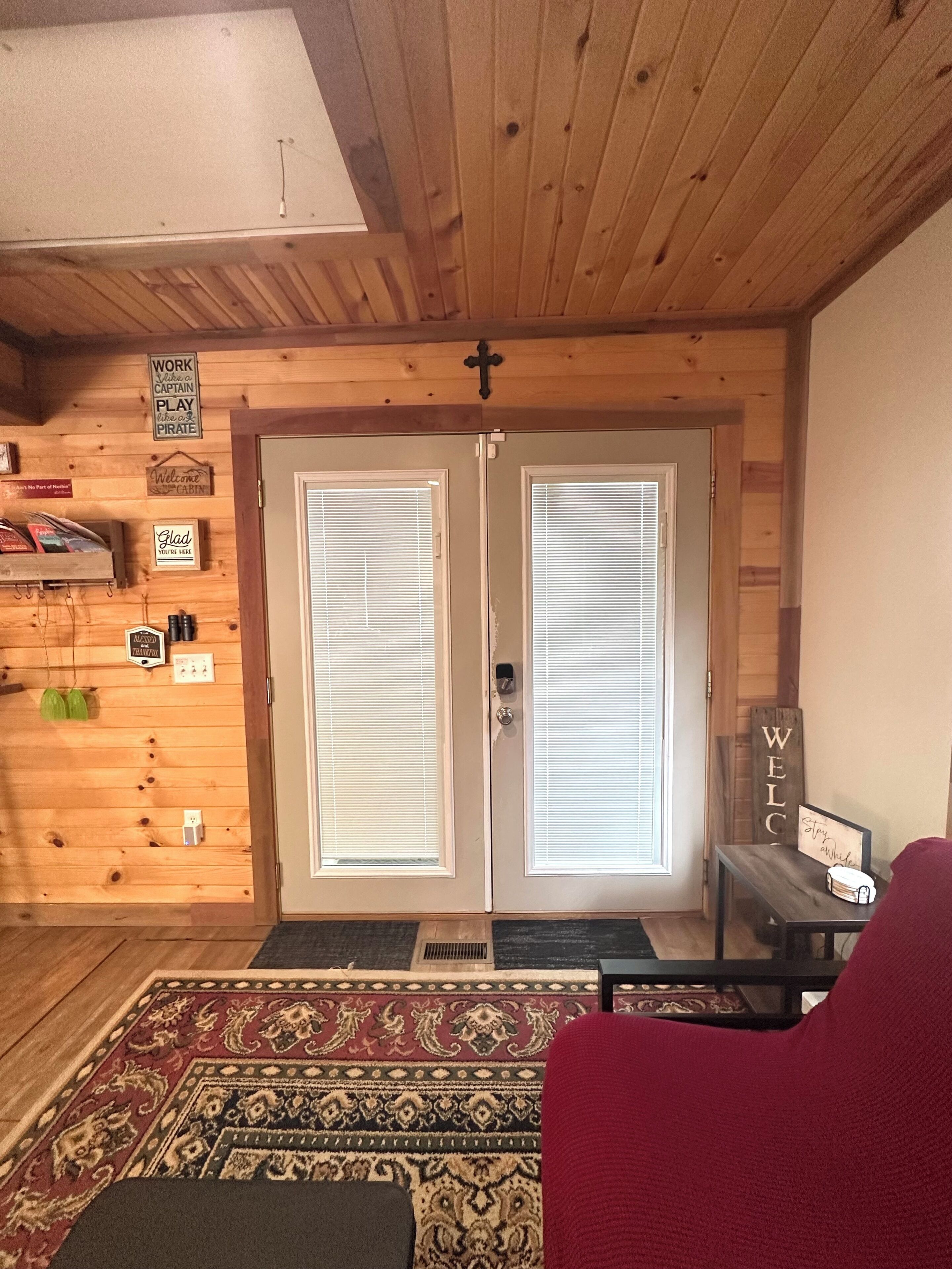 Interno di una baita in legno con una porta doppia, un cartello di benvenuto, un cartello da capo lavoro e un cartello di benvenuti nella baita.