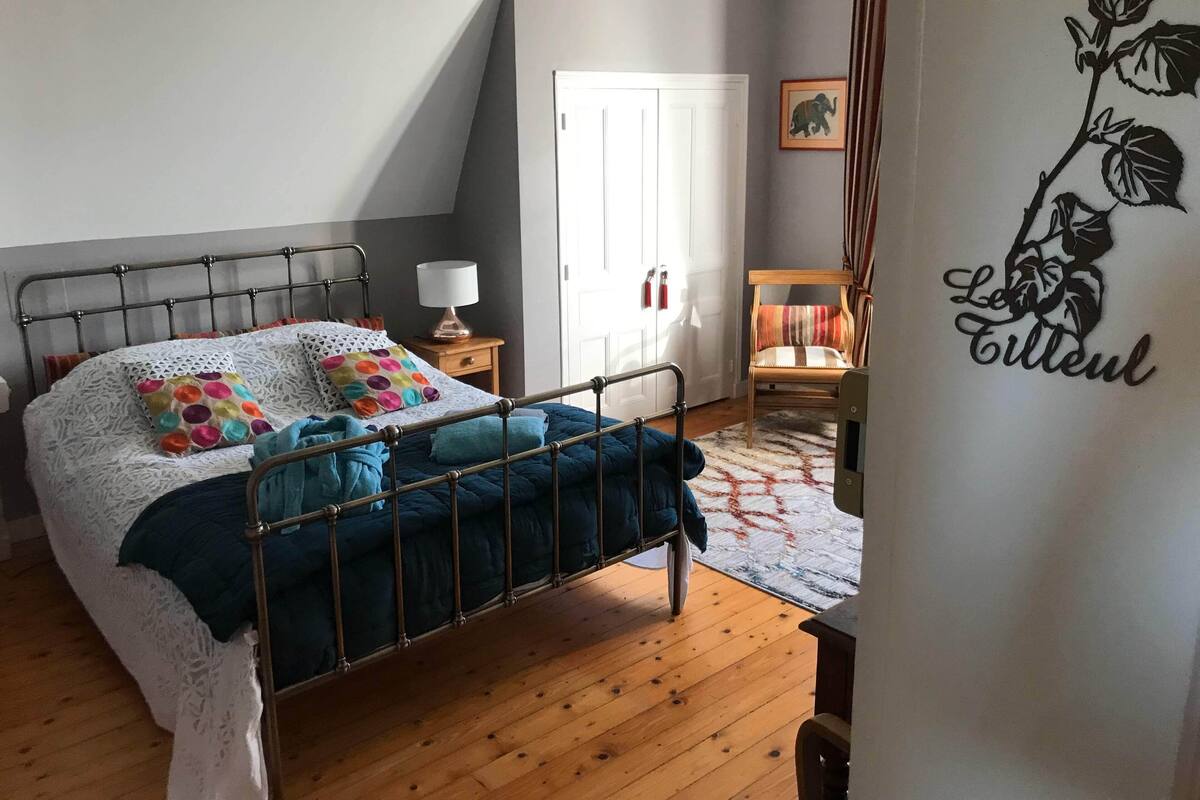 Une chambre à coucher avec un lit en métal, une table de chevet avec une lampe, une chaise et un élément décoratif mural.