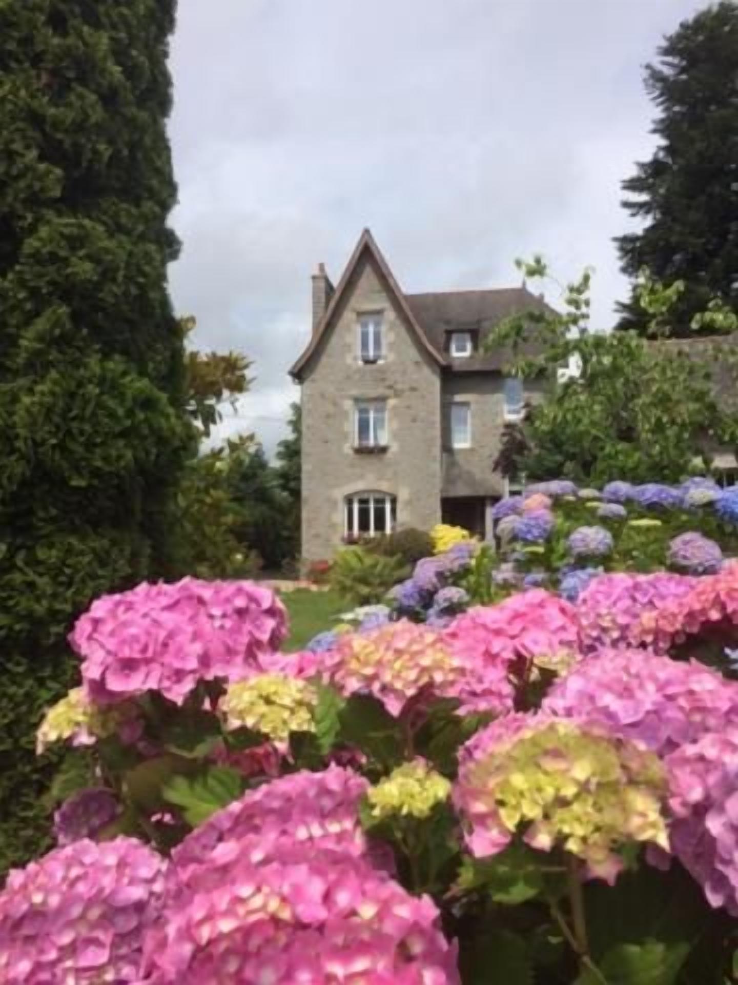 Un edificio con fachada simétrica, una entrada central y un jardín con flores de hortensia.