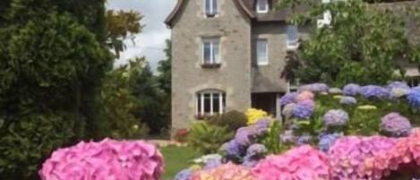 A building with a symmetrical facade, a central entrance, and a garden with hydrangea flowers.