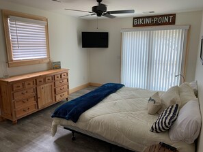 A bedroom with a bed, a dresser, a ceiling fan, a TV, and a sign that reads "BIKINI POINT".