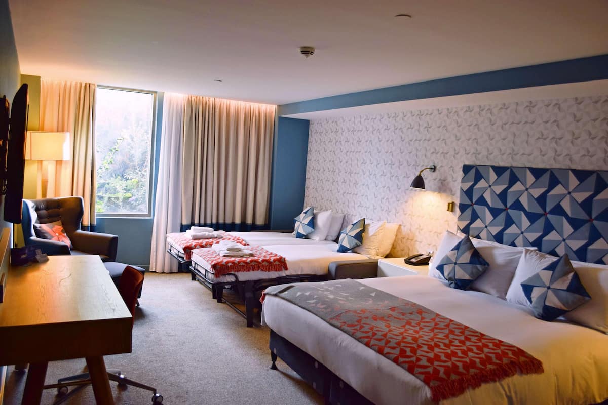 Ein Hotelzimmer mit zwei Betten, einem Schreibtisch, einem Stuhl und einem fensterbelagten Fenster.