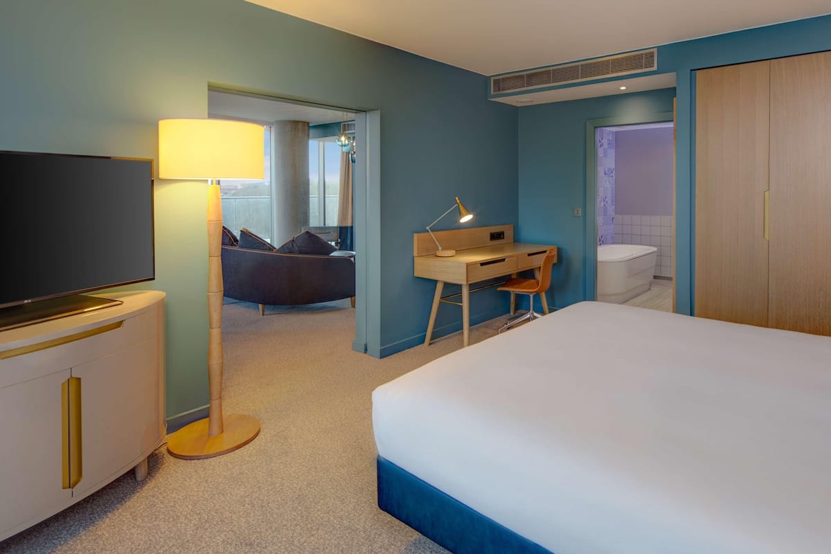 Ein Hotelzimmer mit einem großen Bett, einem Schreibtisch mit Stuhl, einem Fernseher und einem durch eine offene Tür einsehbaren Badezimmer.