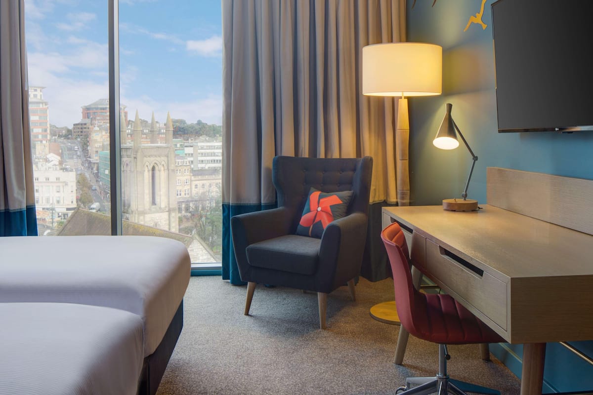 Ein Hotelzimmer mit zwei Betten, einem Schreibtisch, einem Sessel, einer Lampe und einem Fernseher.