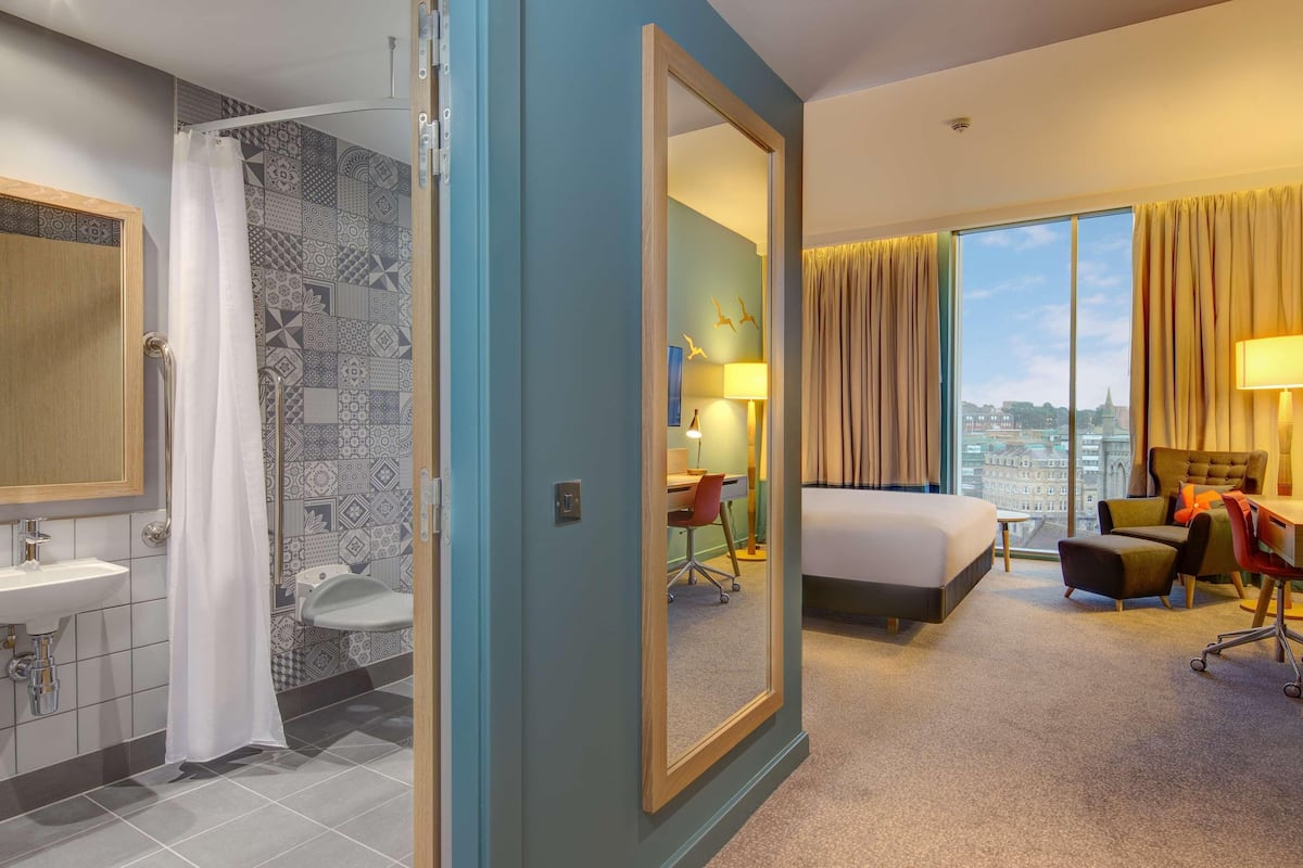 Ein Hotelzimmer mit Bad, Bett, Schreibtisch und Blick auf die Stadt.
