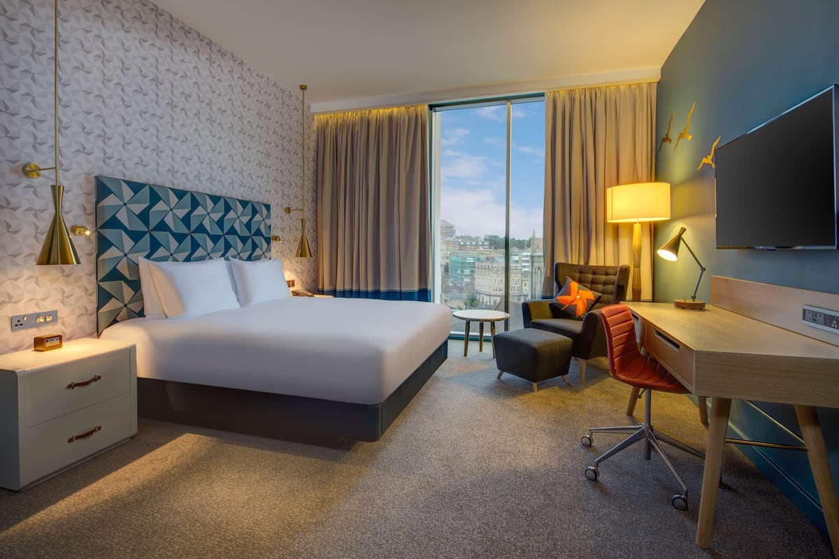 Ein Hotelzimmer mit einem großen Bett, einem Schreibtisch, einem Sessel, einem kleinen Tisch und einem Fernseher.