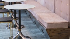 A row of round tables with metal legs, a cushioned bench, and a wall-mounted light fixture. - The Vault Hotel (Houghton)