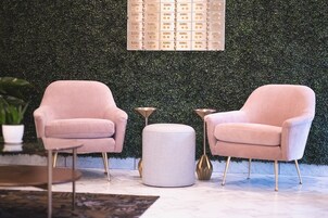 Dos sillones rosas, un reposapiés blanco y una mesita en una habitación con pared verde y suelo estampado.