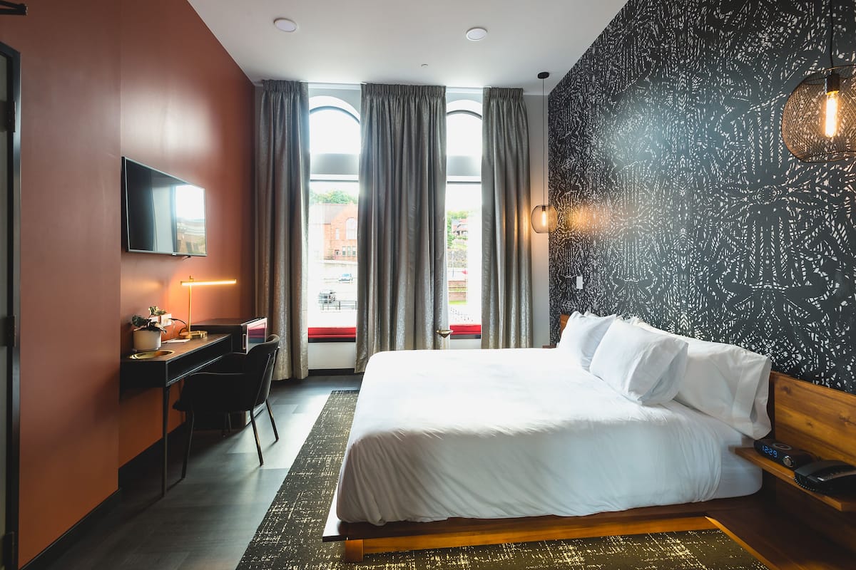 Ein Hotelzimmer mit Bett, Schreibtisch, Stuhl und Fernseher an der Wand.