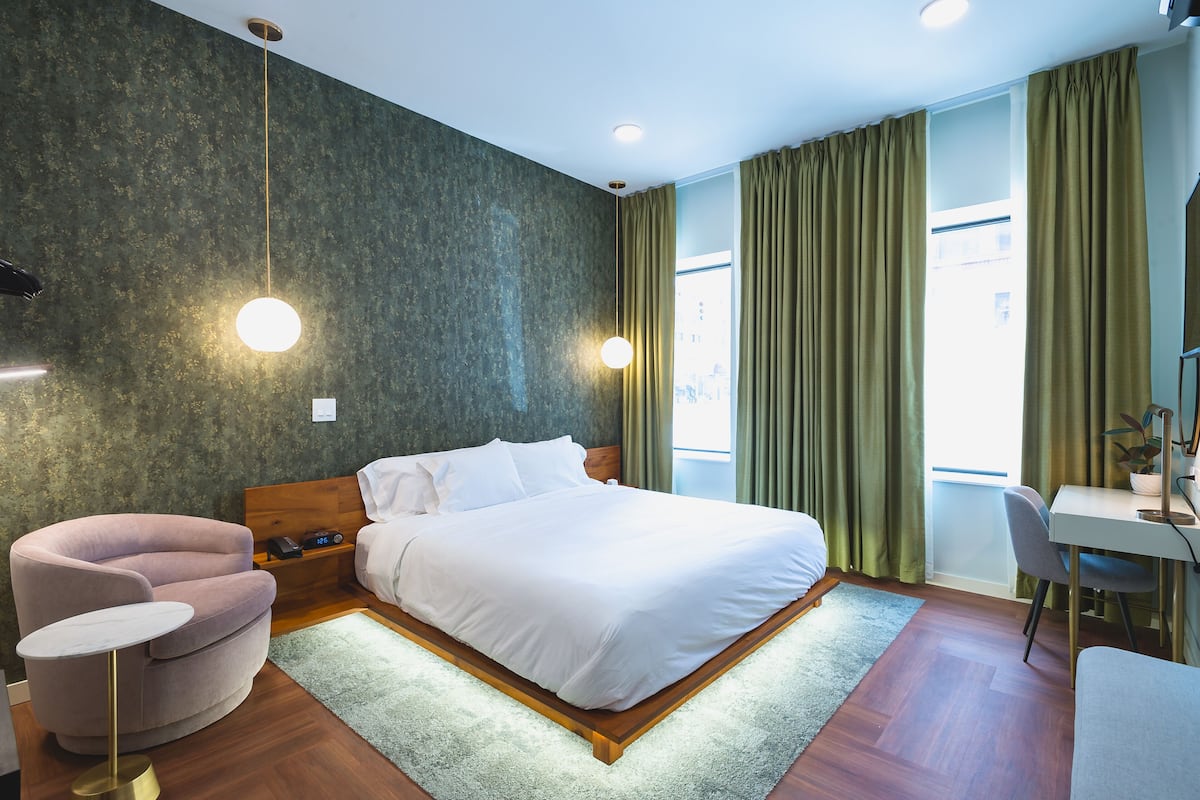 Ein modernes Hotelzimmer mit einem großen Bett, einem Schreibtisch, einem Stuhl und einem kleinen Sessel.