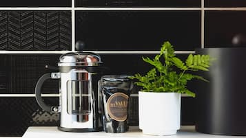 Un comptoir de cuisine avec une machine à café, un récipient de café et une plante en pot.