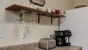 Uma bancada de cozinha com uma torradeira, uma cafeteira e uma estante com copos de vinho e xícaras.
