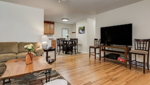 Sala de estar com sofá, mesa de centro, televisão e área de jantar com cadeiras e mesa.