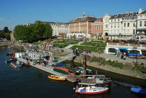 A riverside area with boats docked, a pedestrian bridge, and historic buildings.