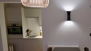 Eine moderne Küche mit integrierten Geräten, ein Essbereich mit Tisch und Stühlen sowie eine wandmontierte Leuchte.