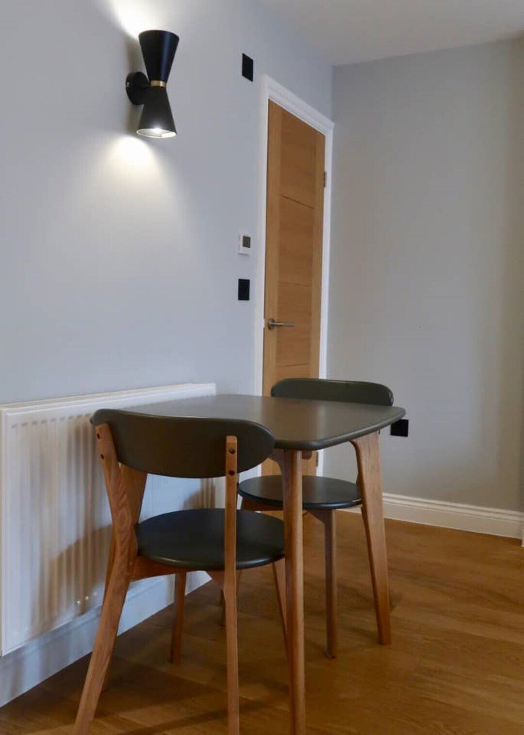 Un comedor con una mesa, sillas, una lámpara de pared y una puerta.