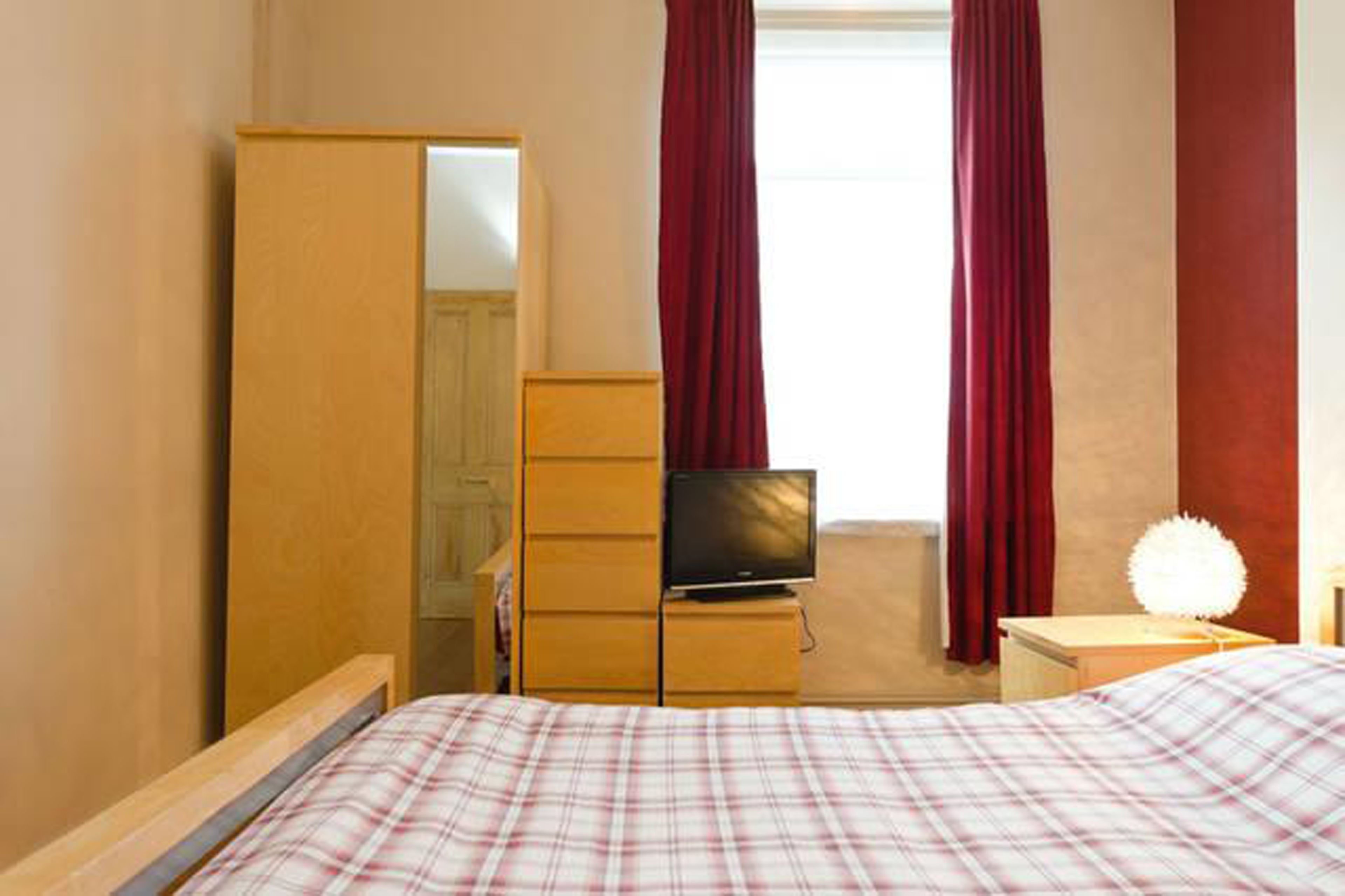 A bedroom with a bed, a dresser, a television, and a lamp.