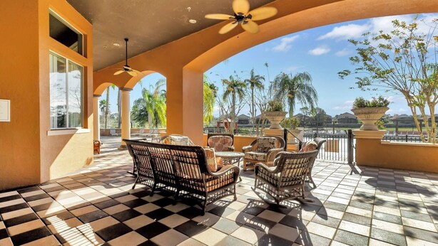 A covered outdoor seating area with wicker furniture, a checkered floor, and a view of palm trees and a body of water. - Impressive Waterfront Retreat Near Disney With Cinema Room - 5bd/4ba PH - Rav5341 (Davenport)