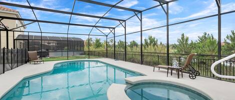 A swimming pool with a hot tub, surrounded by a covered patio with chairs and a table.