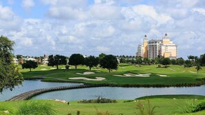 A golf course with a water hazard, trees, and a large hotel in the background. - Stylish NEW Renovation in Reunion Resort - Large Patio and Pool Deck 3bd/3.5ba #3ru456 (Kissimmee)
