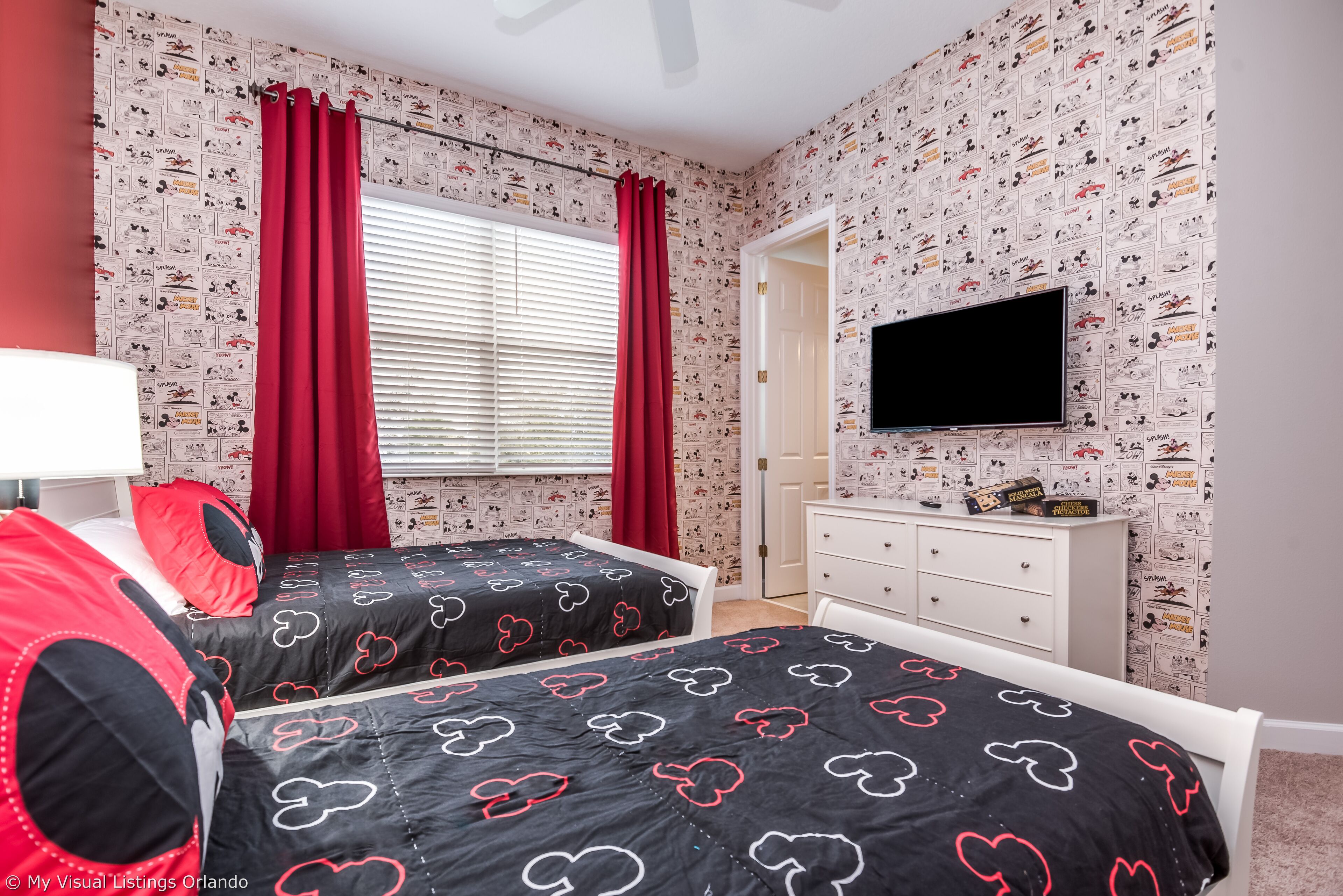 A bedroom with two beds, red curtains, a TV, and a dresser.