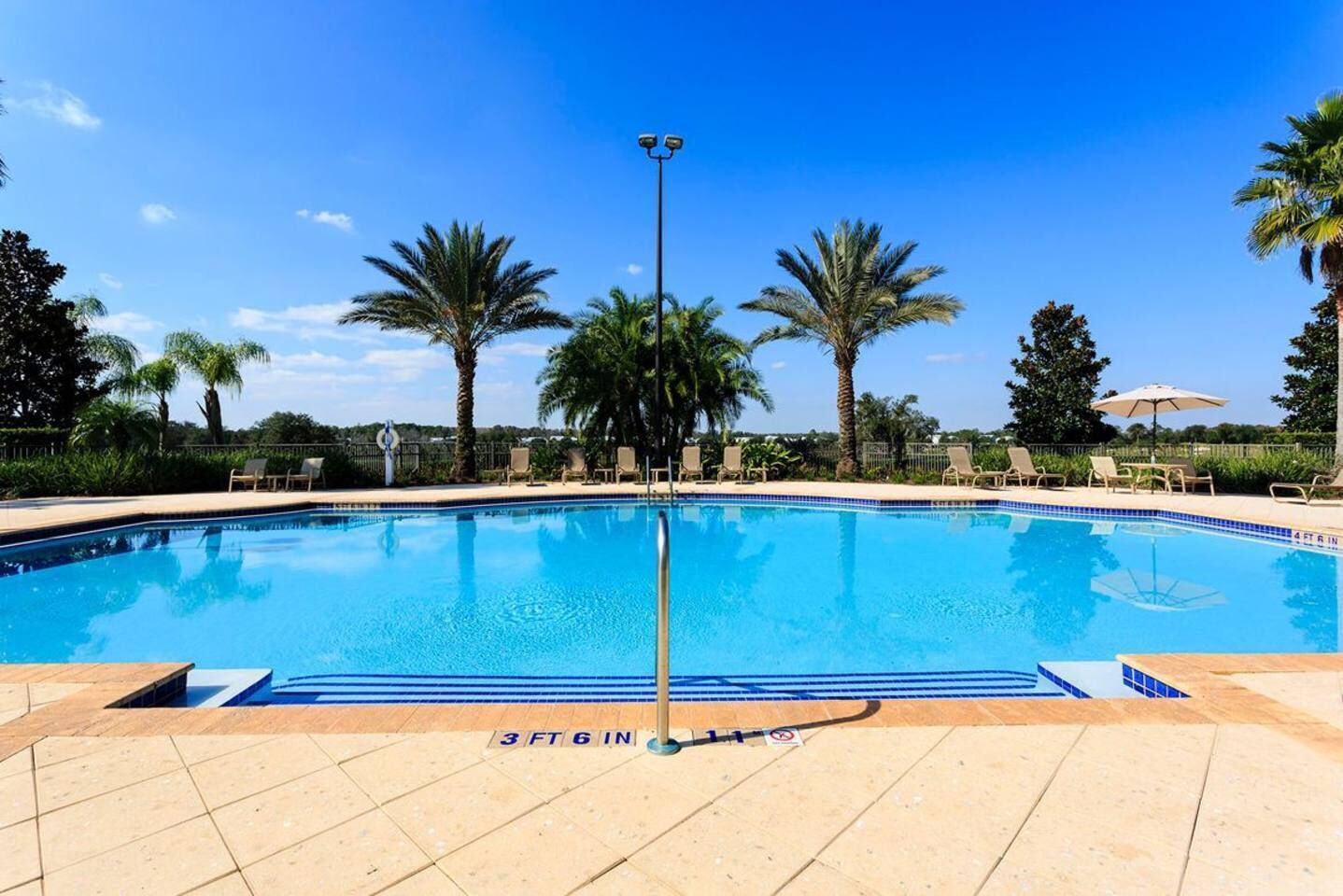 Ein klares, blaues Schwimmbecken mit einer Tiefenmarkierung von 107 Zentimetern, umgeben von Palmen und Liegestühlen.