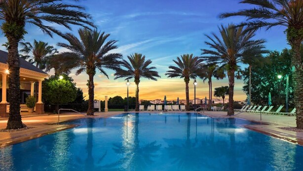 A swimming pool with palm trees and a building in the background. - Stylish NEW Renovation in Reunion Resort - Large Patio and Pool Deck 3bd/3.5ba #3ru456 (Kissimmee)
