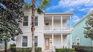 A two-story house with a front porch, a balcony on the second floor, and a well-maintained garden with shrubs and flowers. - Stylish NEW Renovation in Reunion Resort - Large Patio and Pool Deck 3bd/3.5ba #3ru456 (Kissimmee)