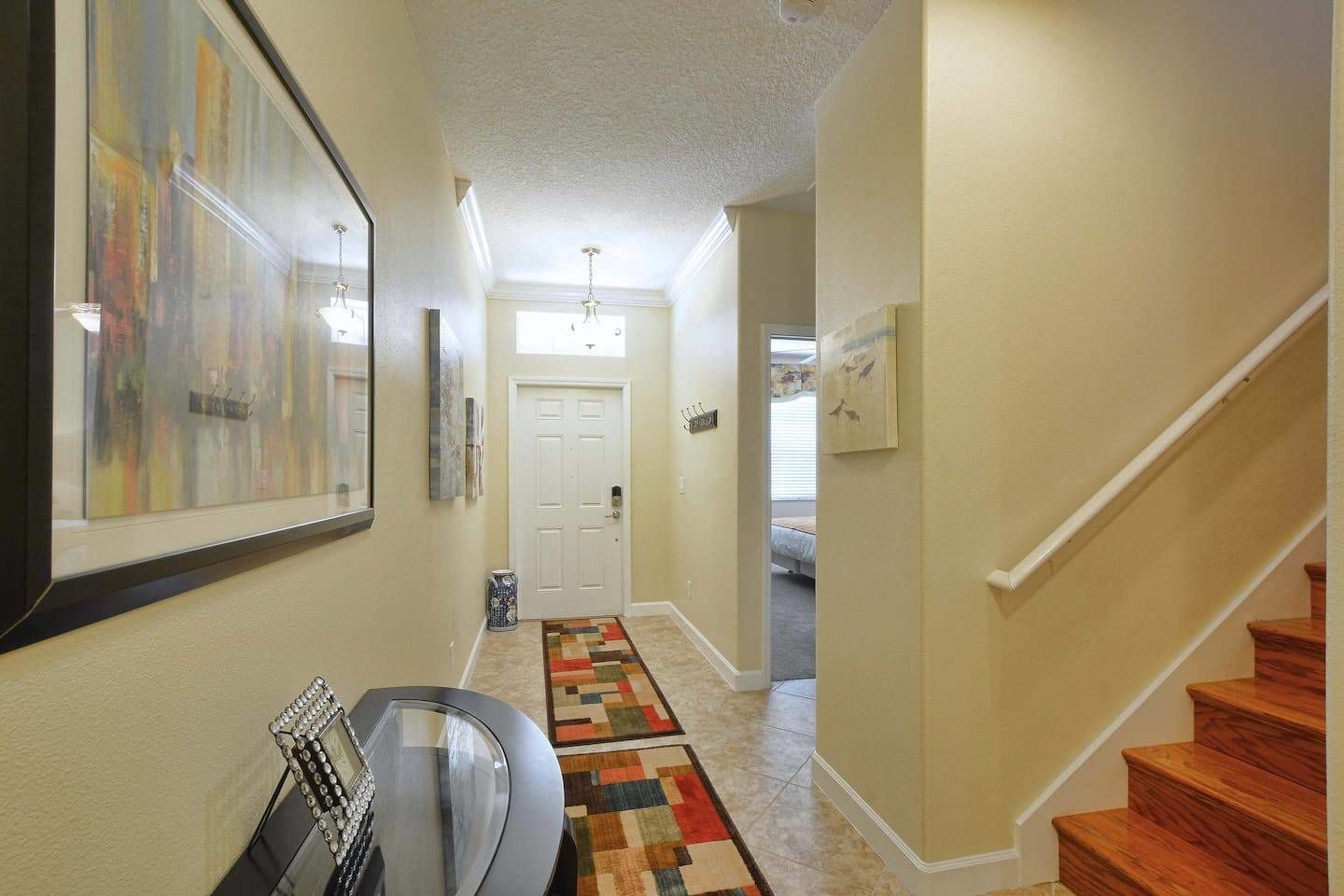 A hallway with a wooden staircase, a door, and a colorful rug.