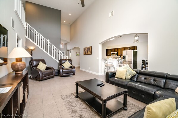 A spacious living room with a black leather sofa, a coffee table, and two leather chairs. A staircase leads to an upper level. - Private Pool Home With Fantastic Upgrades. Very Safe for Children! - 5av534 (Davenport)
