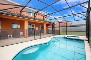 A swimming pool with a glass enclosure, a patio area with chairs, and a view of a building with orange walls. - Enjoy Stunning Sunset Over Lake View! Near Disney #6av131 (Davenport)