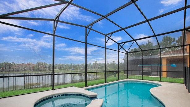 Une piscine avec un jacuzzi, entourée d’une structure en verre, offrant une vue sur un lac et des bâtiments situés au loin.