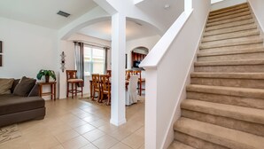 Un vaste espace de vie comprenant un canapé, une table à manger et des chaises, qui donne sur un escalier recouvert de moquette.