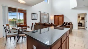 Une cuisine spacieuse dotée d’un grand îlot central, d’un coin repas avec des chaises et d’une vue sur l’extérieur.