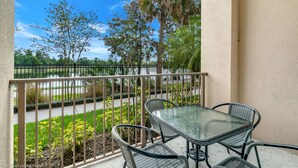 A balcony with a glass table and chairs, overlooking a landscaped area with trees and a pathway. - Stylish and Accessible in Vista Cay With Lake View - 3bd/2ba Condo 3vc114 (Orlando)