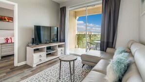 A modern living room with a flat-screen TV, a sofa, a coffee table, and a balcony with a view. - Stylish and Contemporary Vista Cay Hideaway - Lake View 3bd/2ba #3vc4126 (Orlando)