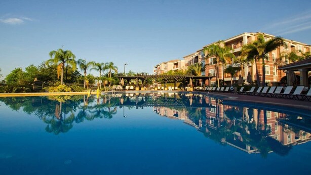 A hotel with a swimming pool, palm trees, and a clear blue sky. - Stylish and Contemporary Vista Cay Hideaway - Lake View 3bd/2ba #3vc4126 (Orlando)