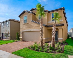 A two-story house with a beige exterior, a garage, and a well-maintained lawn with palm trees. - Breathtaking Spacious Pool Home Near Disney. Star Wars Room! 7BD #7st485 (Davenport)