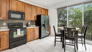 A modern kitchen with wooden cabinets, a black refrigerator, a microwave, and a stove. There is a dining table with chairs and a view of trees through large windows. - NEW Tastefully Designed Town Home. Close to Attractions, Steps From Convention Center! 3br/3ba #3vc138 (Orlando)