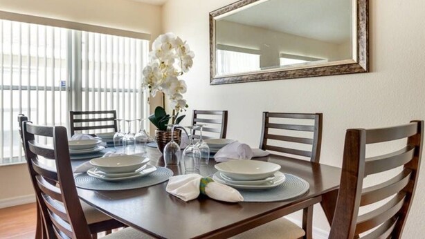A dining area with a round table set for four, surrounded by wooden chairs. A large mirror hangs on the wall above the table. - Comfy and Spacious Near Disney With Pool - 4bd/3ba #4hl124 (Davenport)