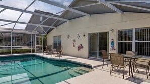 A covered outdoor swimming pool area with a glass roof, a patio with chairs, and a sliding glass door leading to a covered patio area. - Comfy and Spacious Near Disney With Pool - 4bd/3ba #4hl124 (Davenport)