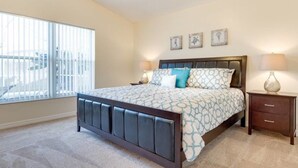 A bedroom with a large bed, a nightstand, a window with blinds, and three wall-mounted pictures. - Comfy and Spacious Near Disney With Pool - 4bd/3ba #4hl124 (Davenport)