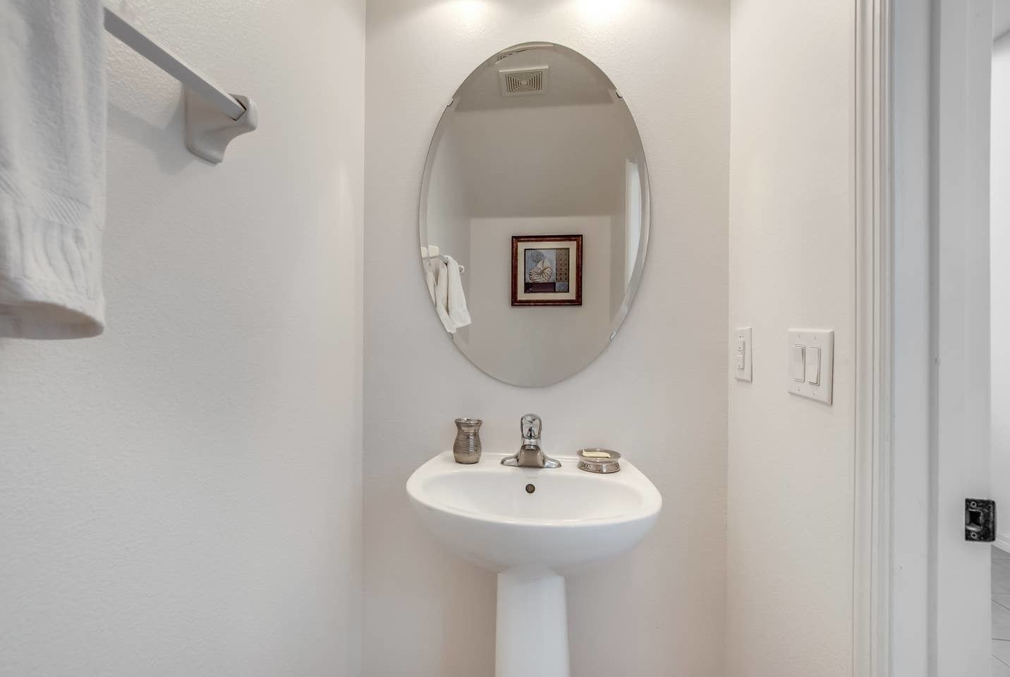 A bathroom with a white sink, a round mirror, and a framed picture on the wall.