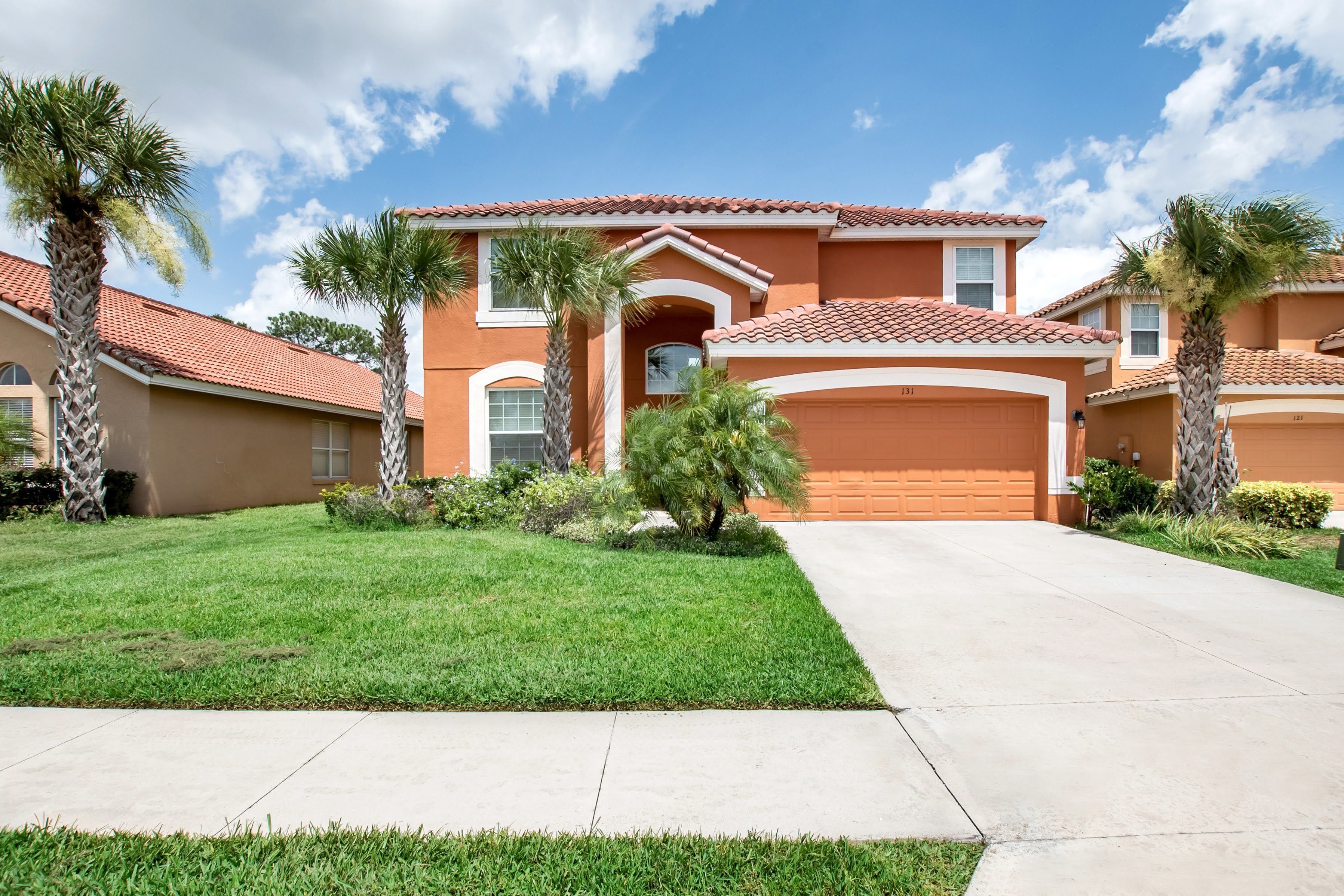 A residential house with a red-tiled roof, a garage, and a well-maintained lawn with palm trees.